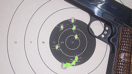 Overhead image of Handgun laying on top of paper target with multiple bullet holes in it